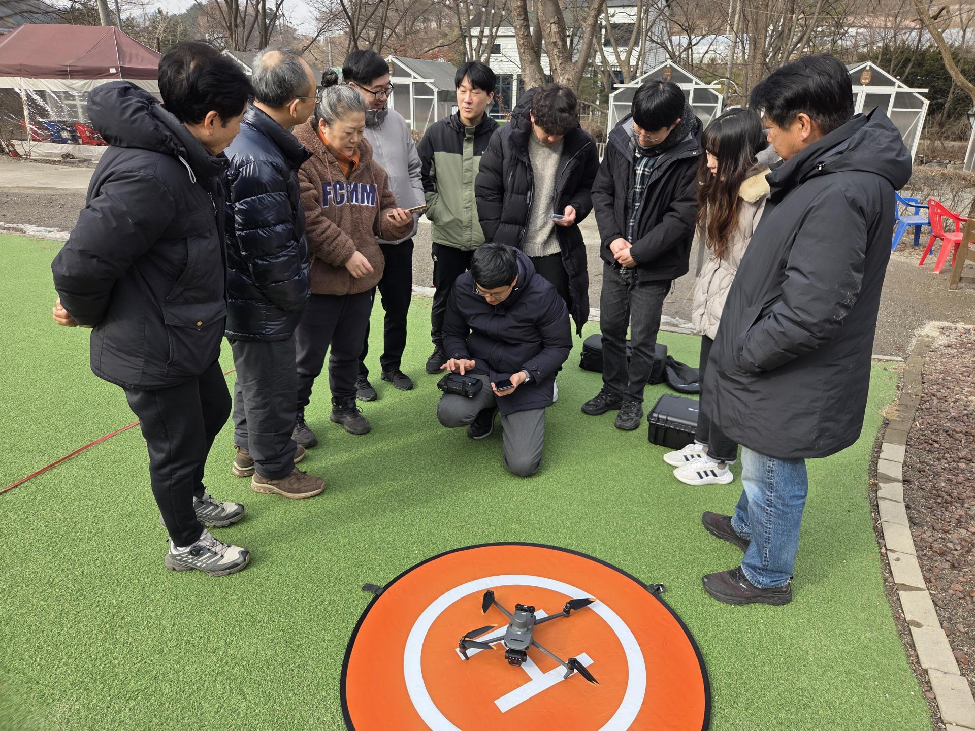 착륙패드에 놓인 드론을 둘러싸고 조작법을 배우는 직원들