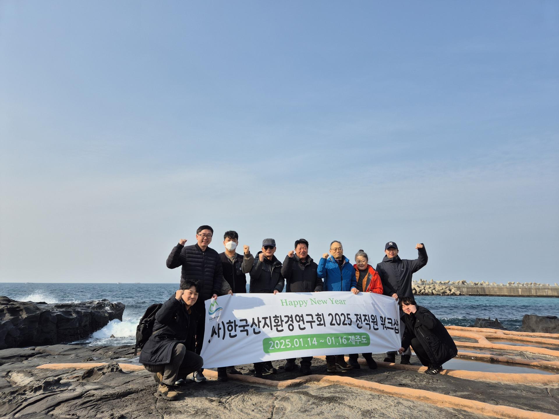해안 방파제를 배경으로 현수막을 들고 기념하는 직원들