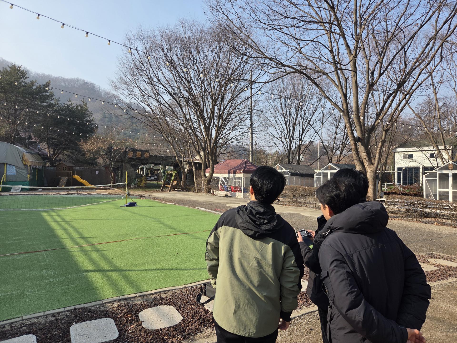 겨울 야외 잔디 운동장에서 드론 실습을 참관하는 직원들