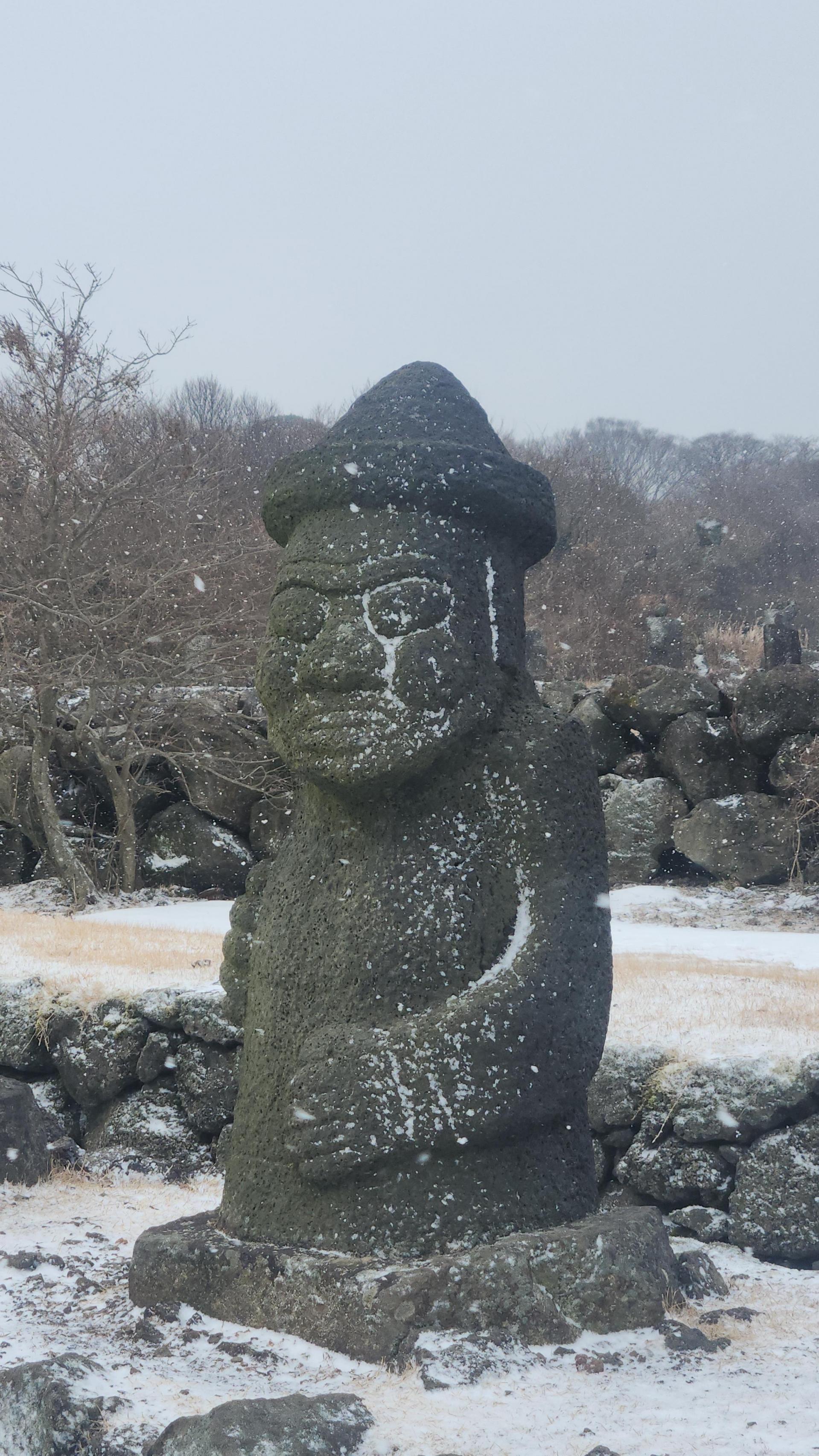 눈 덮인 돌담 앞의 돌하르방 석상